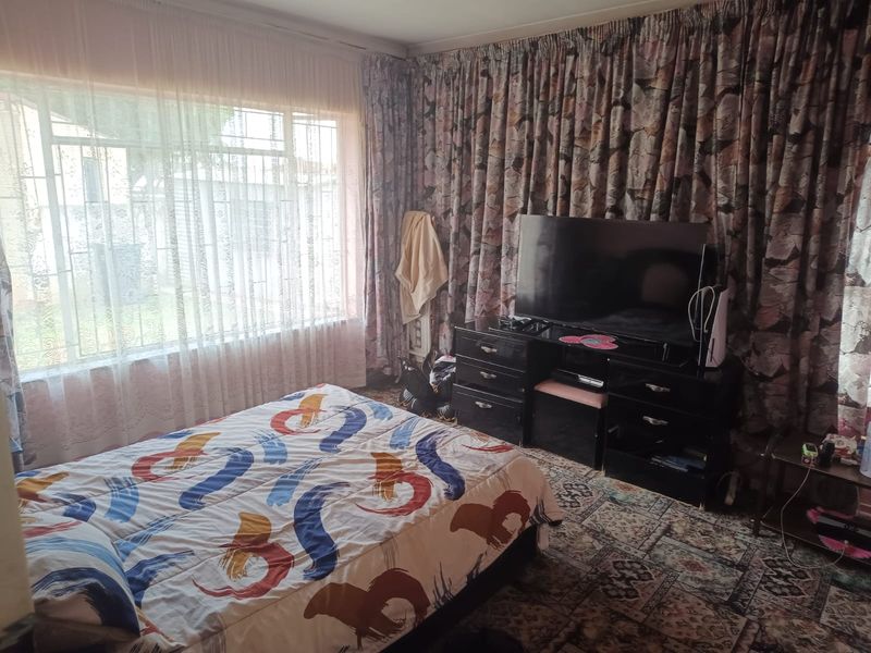A bedroom featuring a large window with security bars and full-length curtains, providing natural light and a view of the exterior.