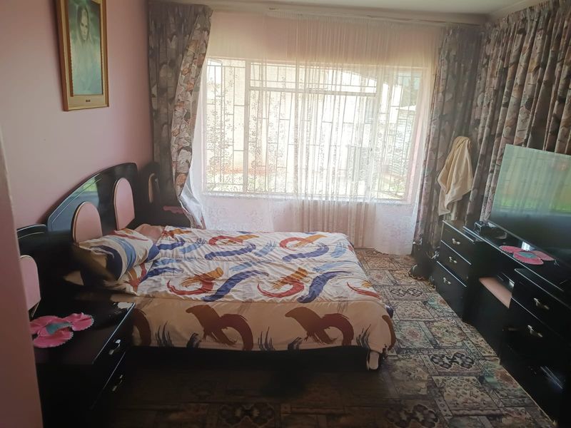 A bedroom featuring carpeted flooring and a large window fitted with security bars, offering natural light.