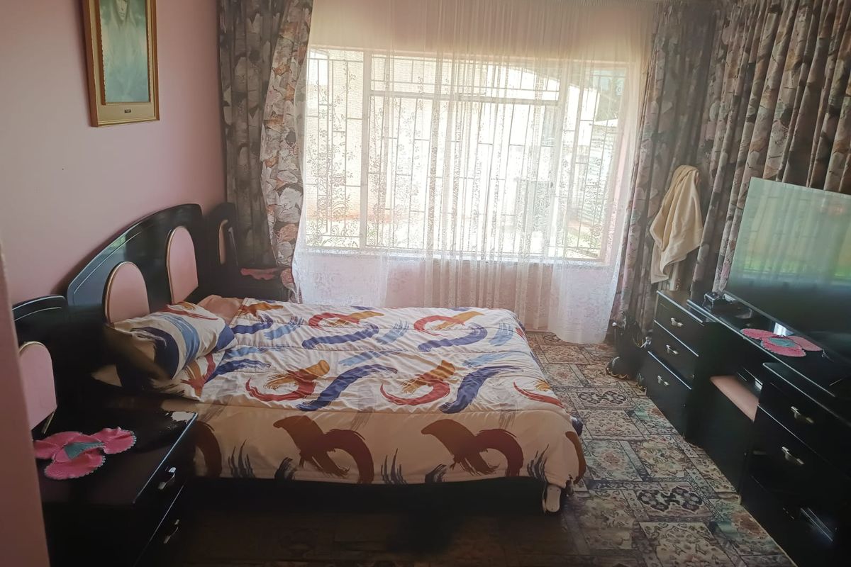 A bedroom featuring a large window with security bars and patterned carpet flooring, offering a functional space with potential for modernization.
