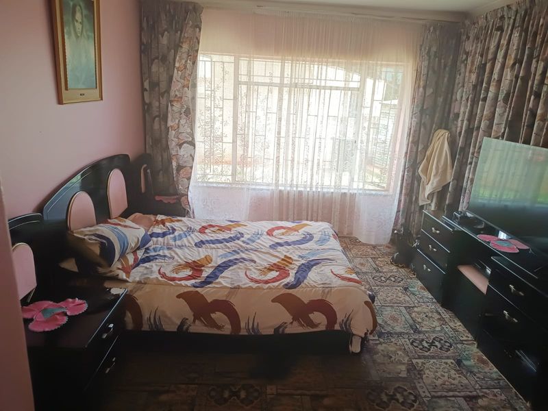 A bedroom featuring a large window with security bars and patterned carpet flooring, offering a functional space with potential for modernization.