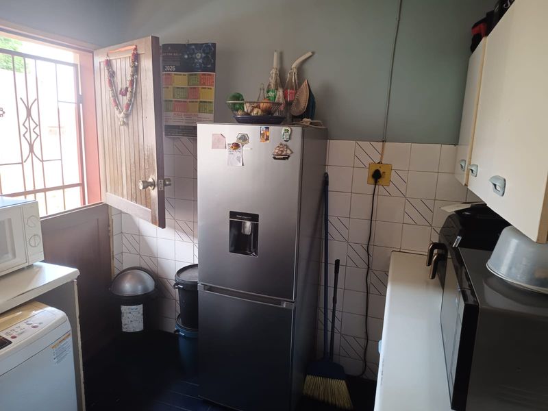 A compact kitchen area featuring tiled splashbacks, fitted cabinetry, and direct access to an exterior door with a security gate.