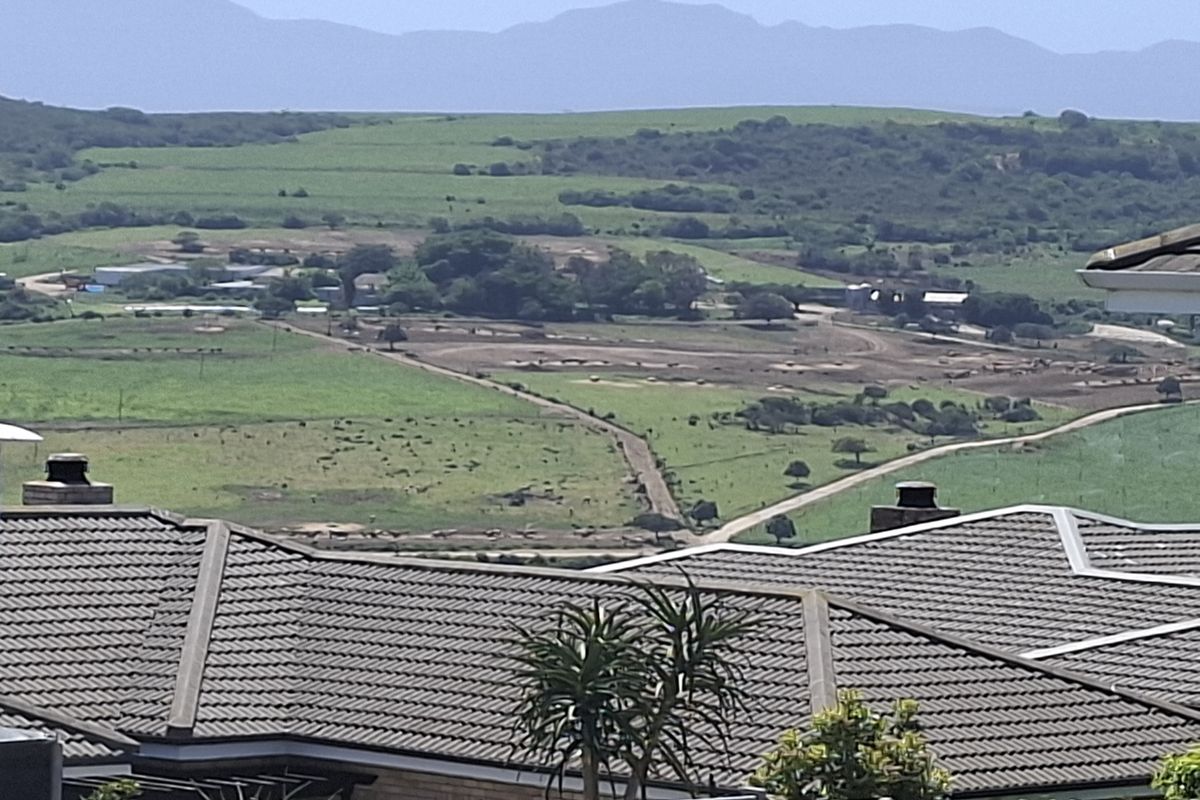 Elevated view overlooking a rural landscape with rolling green hills and distant mountains, featuring residential tiled roof structures in the foreground.