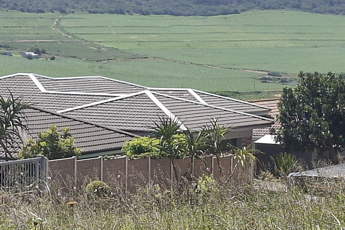 An elevated view of a residential property featuring a tiled roof and boundary wall, overlooking expansive green agricultural fields.