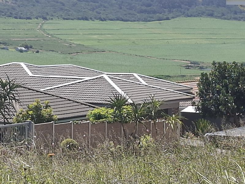 An elevated view of a residential property featuring a tiled roof and boundary wall, overlooking expansive green agricultural fields.