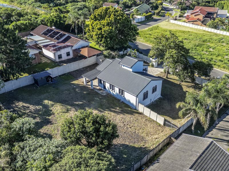 Aerial view of a residential property featuring a metal roof, spacious yard, perimeter wall, and gated driveway access within a suburban neighborhood.