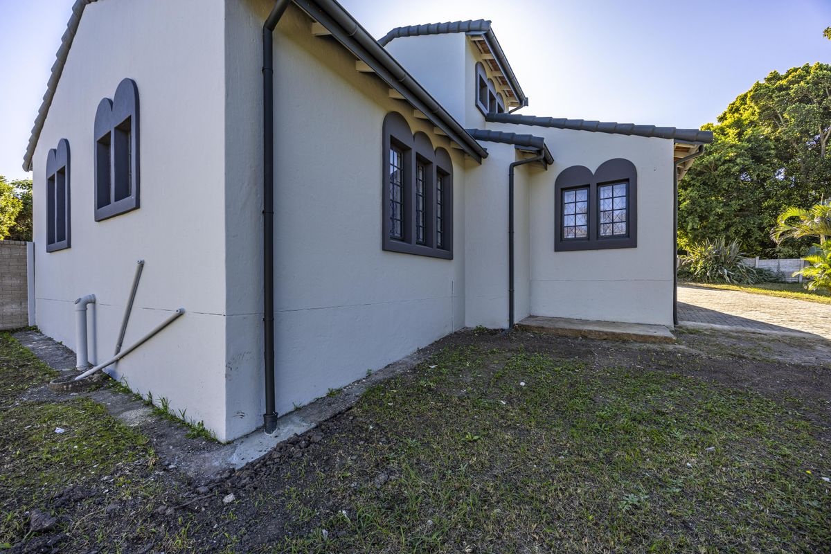 Rear exterior view of the house featuring plastered walls, dark-framed leaded glass windows, and a tiled roof with functional guttering.