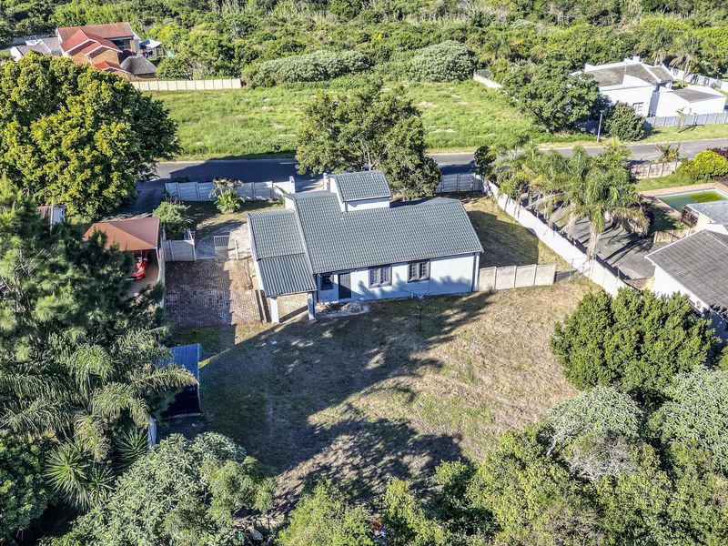 Aerial view of a residential property featuring a tiled roof, paved driveway, carport, and surrounding garden space within a suburban neighborhood.