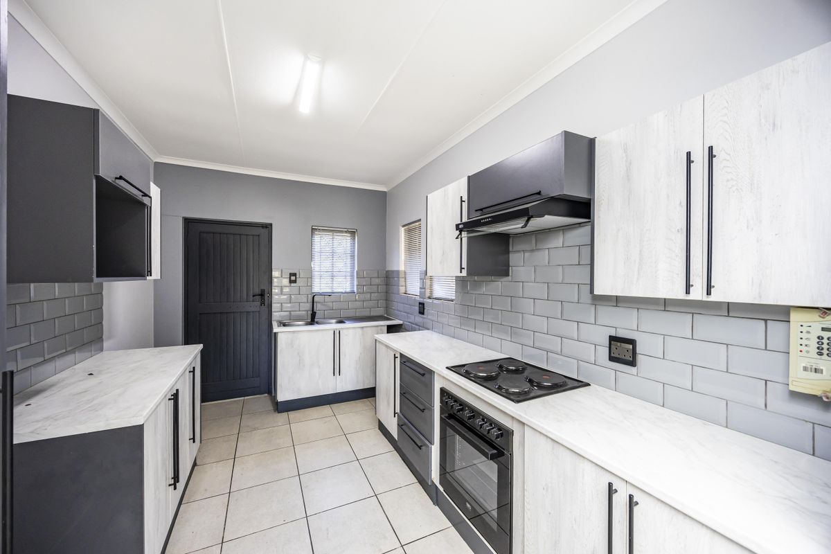 Modern kitchen featuring light wood-grain cabinetry, subway tile backsplash, built-in oven and hob, and neutral tiled flooring.
