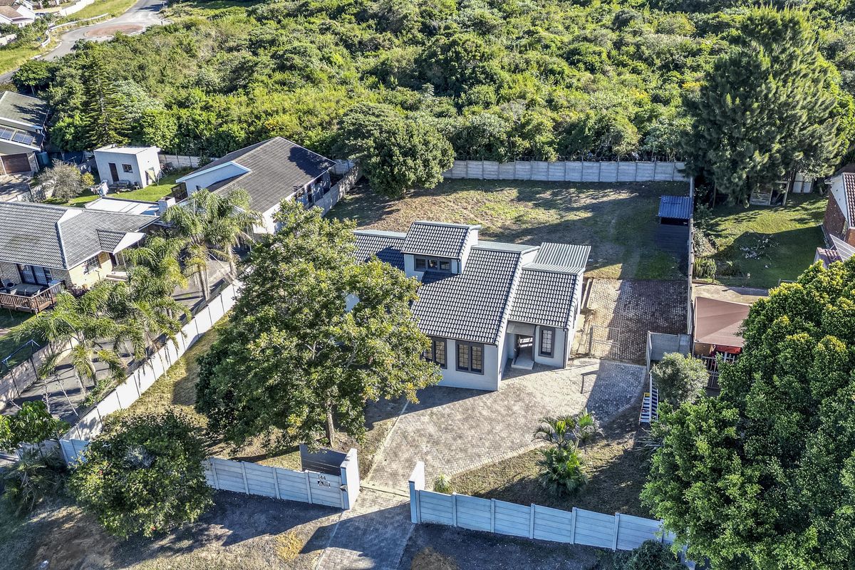 Aerial view of a residential property featuring a tiled roof house, paved driveway, and established garden within a fenced perimeter.