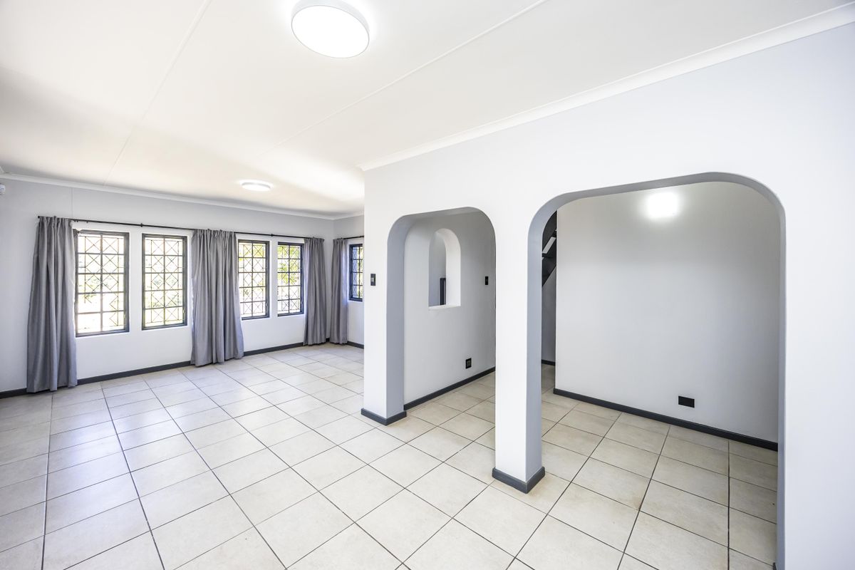Spacious, light-filled living area featuring neutral tiled flooring, distinctive arched architectural details, and classic leaded glass windows.