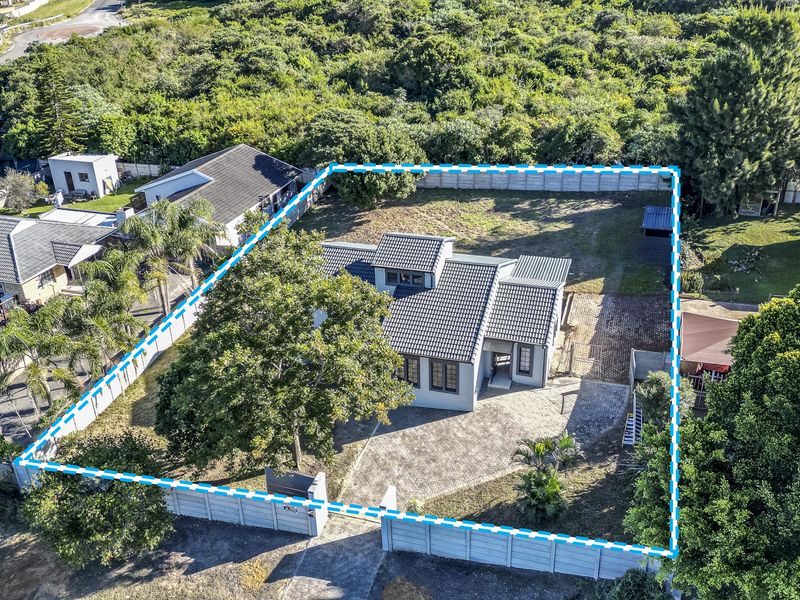 Aerial view of a residential property featuring a tiled roof house, paved driveway, and a spacious garden enclosed by perimeter walls.