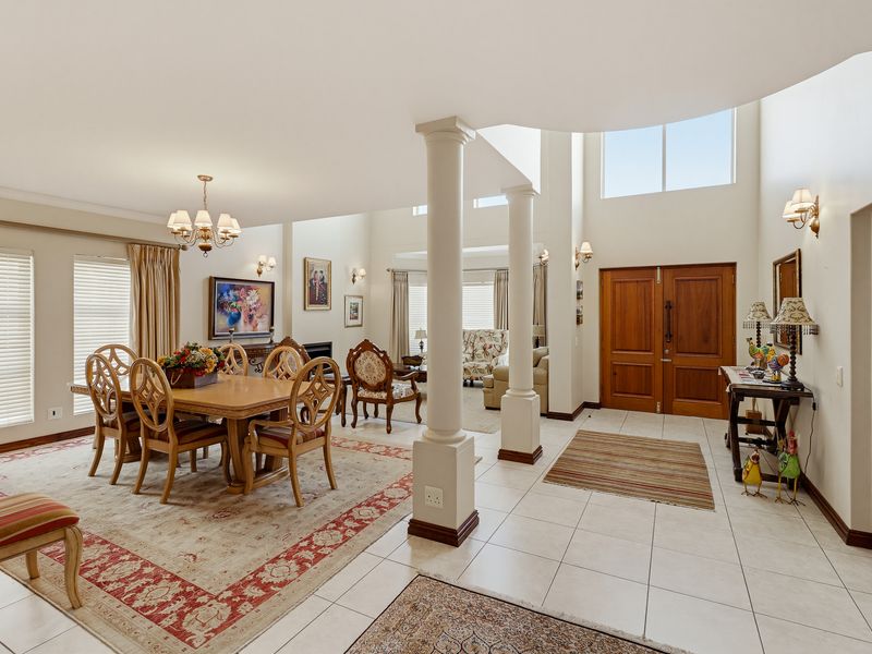 Spacious open-plan living and dining area featuring high ceilings, structural columns, tiled flooring, and double wooden entrance doors with natural light.
