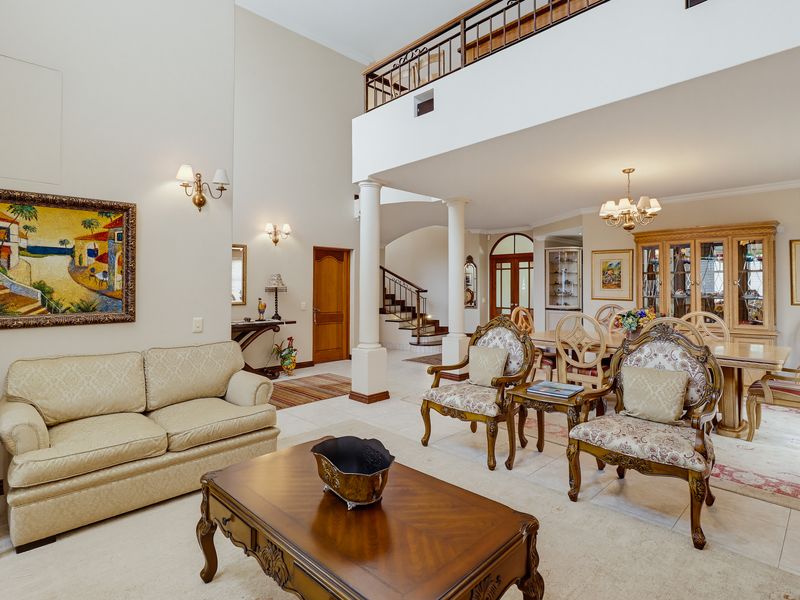 Spacious open-plan living and dining area featuring double-volume ceilings, a mezzanine level with wrought iron balustrades, and elegant structural columns.