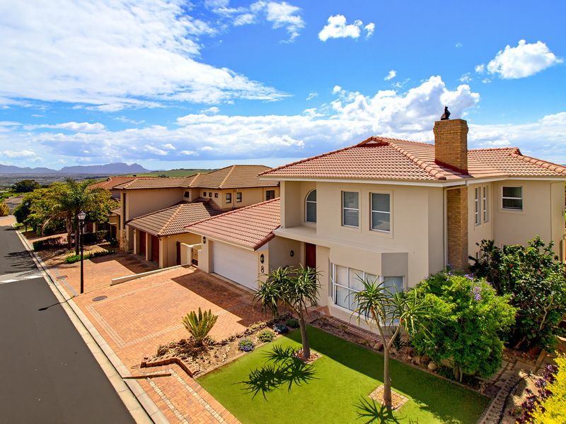 A well-maintained two-story residential property featuring a tiled roof, brick chimney, paved driveway, and an integrated double garage with a landscaped front garden.