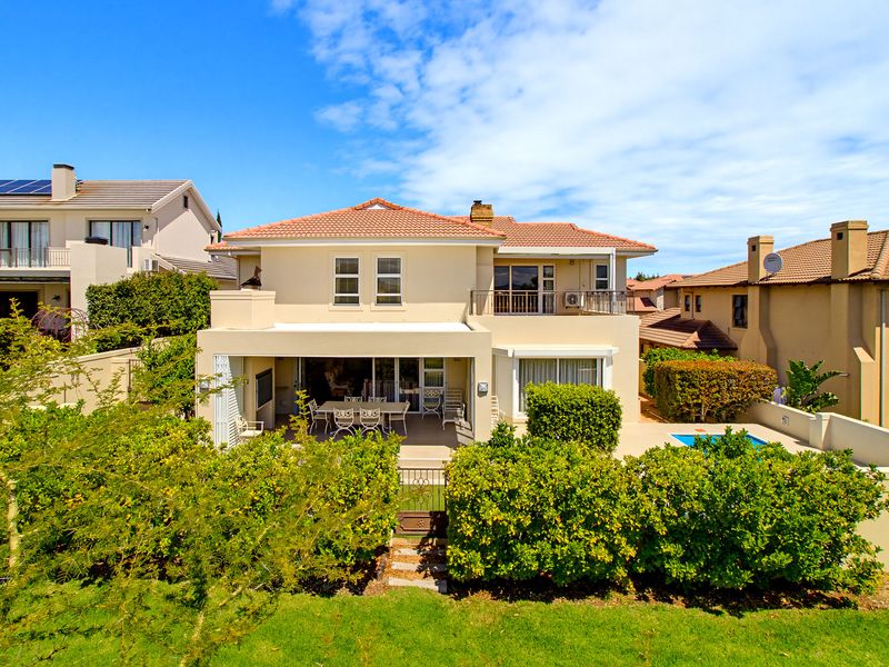Rear view of a two-story residential property featuring a covered patio, balcony, swimming pool, and well-maintained garden area.