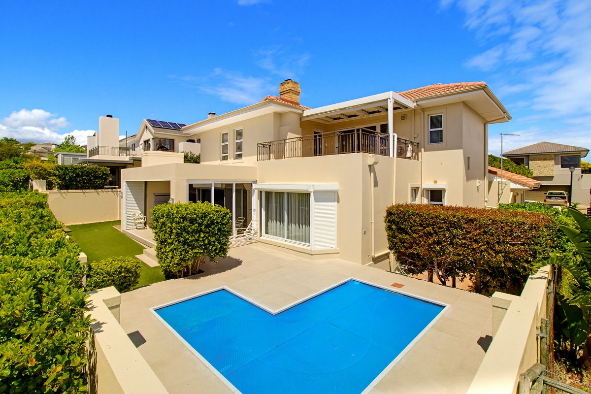 Rear view of the property featuring a swimming pool with cover, a paved patio area, and an upper-level balcony with metal railings.