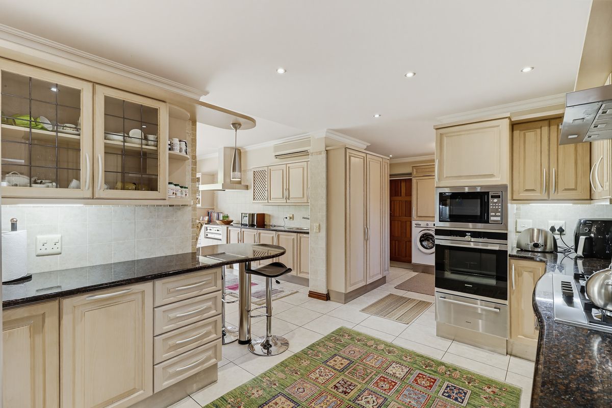 Spacious kitchen featuring light-toned cabinetry, granite countertops, integrated appliances, and a breakfast bar, with an adjacent laundry area visible.