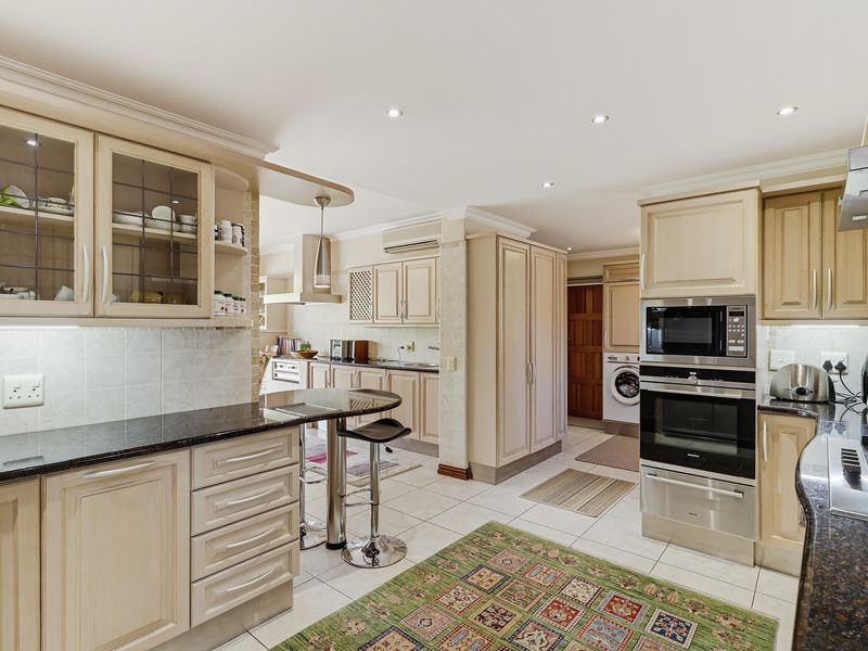 Spacious kitchen featuring light-toned cabinetry, granite countertops, integrated appliances, and a breakfast bar, with an adjacent laundry area visible.