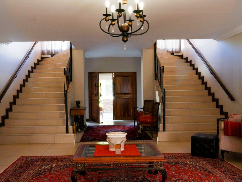 Grand entrance hall featuring a symmetrical dual staircase with wrought iron balustrades, tiled flooring, and a central chandelier.