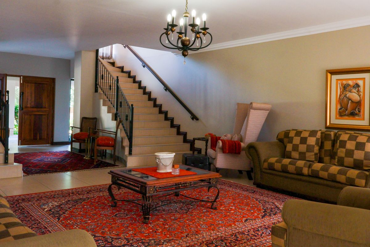 Spacious living area featuring a prominent staircase with a wrought iron balustrade, tiled flooring, and elegant cove cornicing.