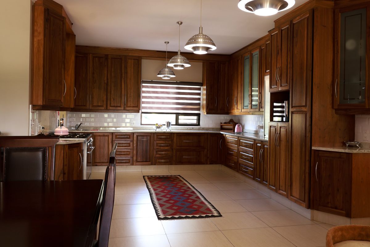 Spacious kitchen featuring extensive wooden cabinetry, stone countertops, subway tile backsplash, and modern pendant lighting, offering a warm and functional culinary space.
