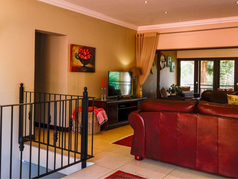 A spacious living area featuring tiled flooring, crown molding, recessed lighting, and a wrought iron staircase railing, with direct access to an outdoor patio area.
