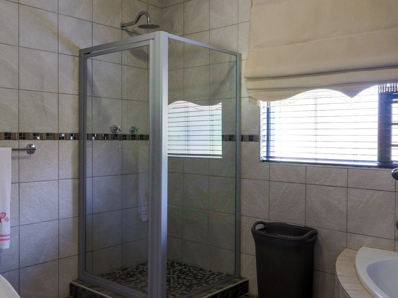 A functional bathroom featuring a glass-enclosed shower, a built-in bathtub, and neutral wall tiling with a decorative mosaic accent border.