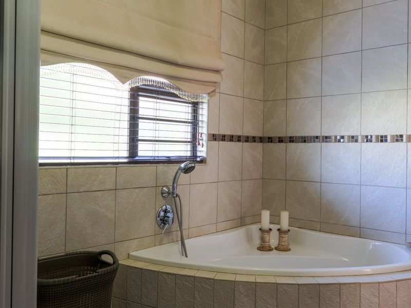 A well-maintained bathroom featuring a corner bathtub with a handheld shower mixer, complemented by neutral ceramic wall tiles and a decorative mosaic border.