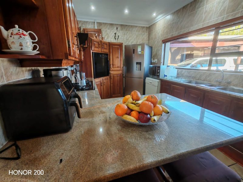 A functional kitchen featuring warm-toned wooden cabinetry, granite countertops, a double sink, and a tiled backsplash with integrated built-in oven.