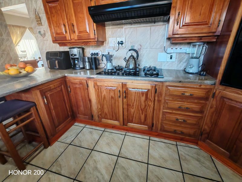A functional kitchen featuring warm-toned wooden cabinetry, granite countertops, a gas hob with an extractor fan, and tiled flooring.
