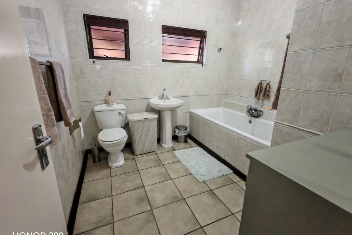A functional bathroom featuring a pedestal basin, toilet, and bathtub with neutral wall and floor tiling.