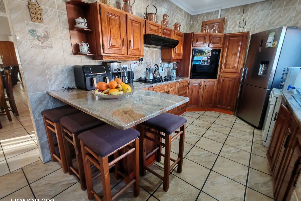 A functional kitchen featuring warm-toned wooden cabinetry, granite countertops, a built-in oven, and a gas hob with a tiled backsplash and flooring.