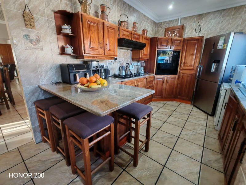 A functional kitchen featuring warm-toned wooden cabinetry, granite countertops, a built-in oven, and a gas hob with a tiled backsplash and flooring.