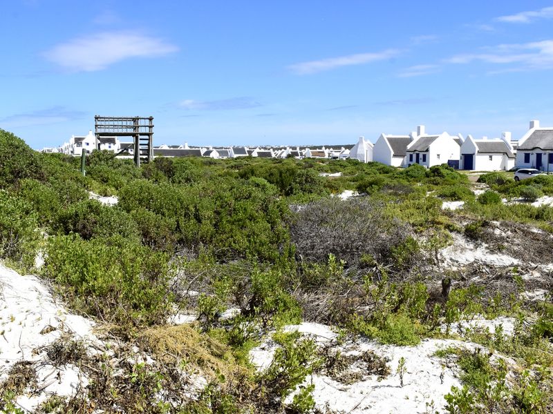 A scenic view of a coastal residential area featuring natural sandy terrain, native vegetation, and a wooden observation structure.