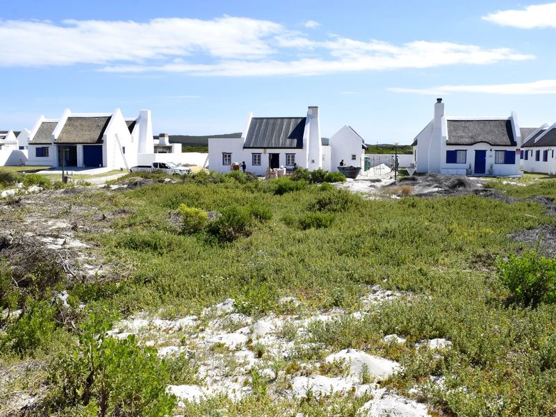 A view of a residential development featuring multiple white cottages with thatched roofs and blue shutters set within a natural coastal landscape.