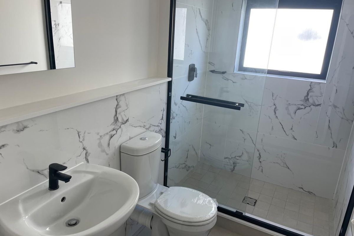 Modern bathroom featuring marble-look wall tiles, a glass-enclosed shower with black fixtures, a pedestal basin, and a dual-flush toilet.