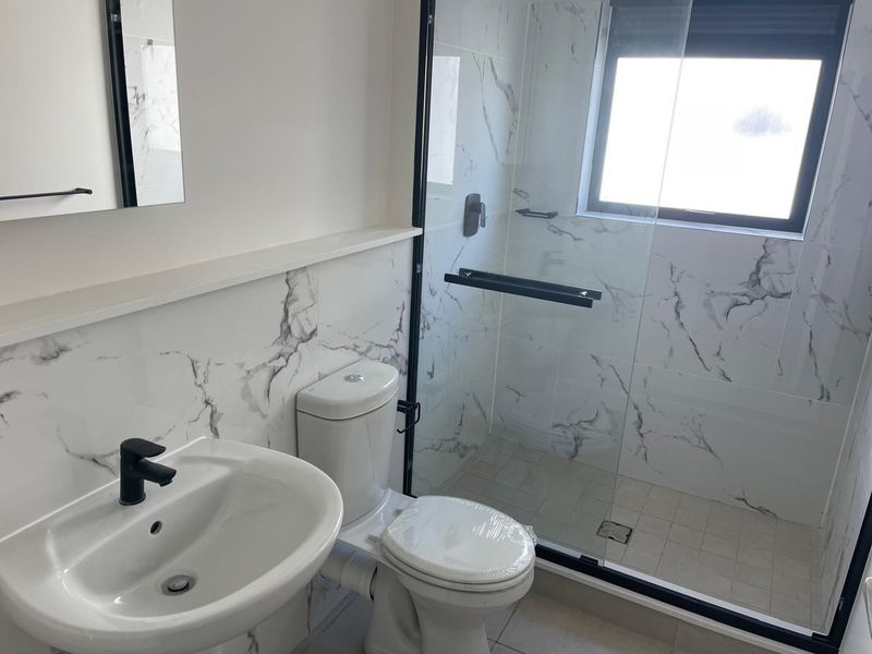Modern bathroom featuring marble-look wall tiles, a glass-enclosed shower with black fixtures, a pedestal basin, and a dual-flush toilet.