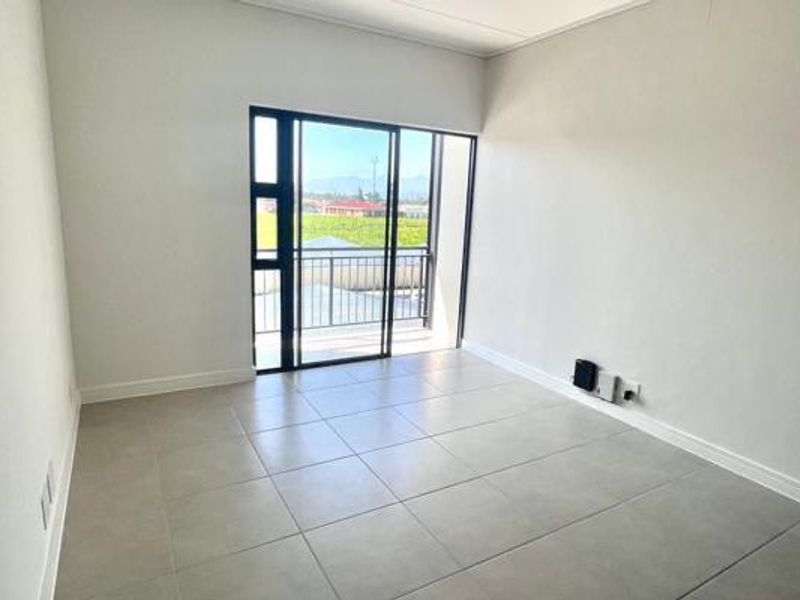 A bright, empty living area featuring neutral tiled flooring and a large sliding glass door providing access to a balcony with scenic views.