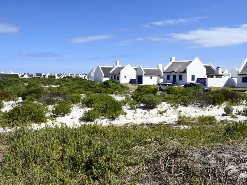 A view of a coastal residential development featuring traditional white cottages with thatched roofs set within a natural sandy landscape.