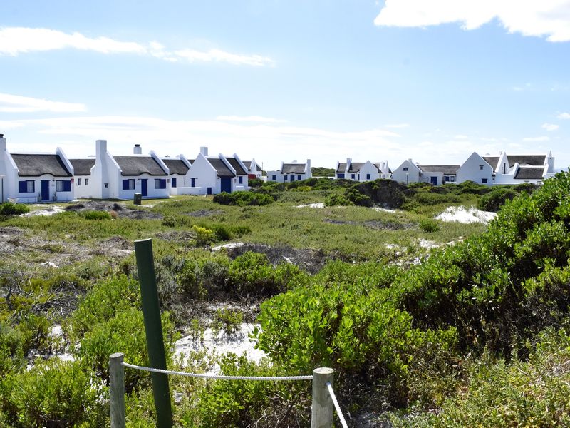 A view of a residential estate featuring multiple white cottages with traditional thatched roofs set within a natural coastal landscape.