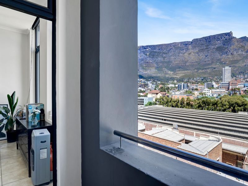A balcony featuring a metal balustrade and tiled flooring, offering an expansive view of the city and mountain landscape.