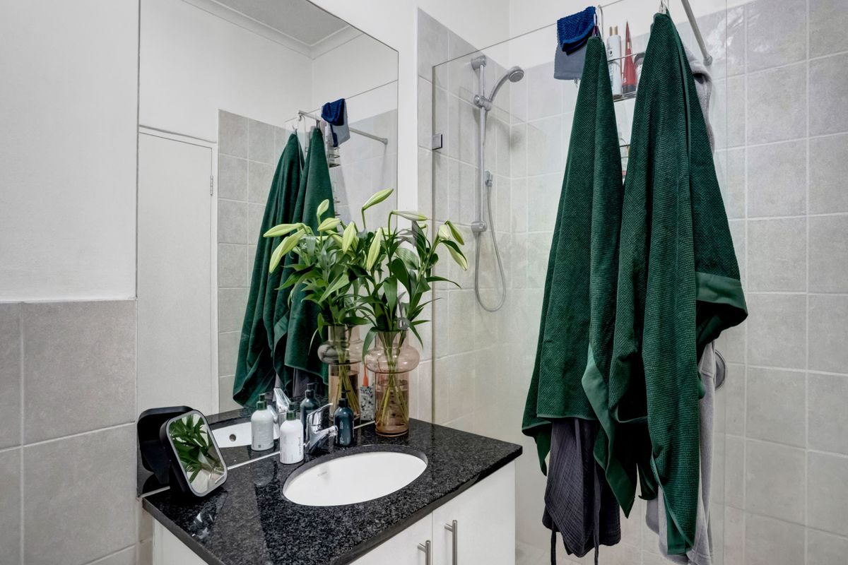 Modern bathroom featuring a granite-topped vanity with an undermount sink, a large wall mirror, and a glass-enclosed shower with ceramic tiling.