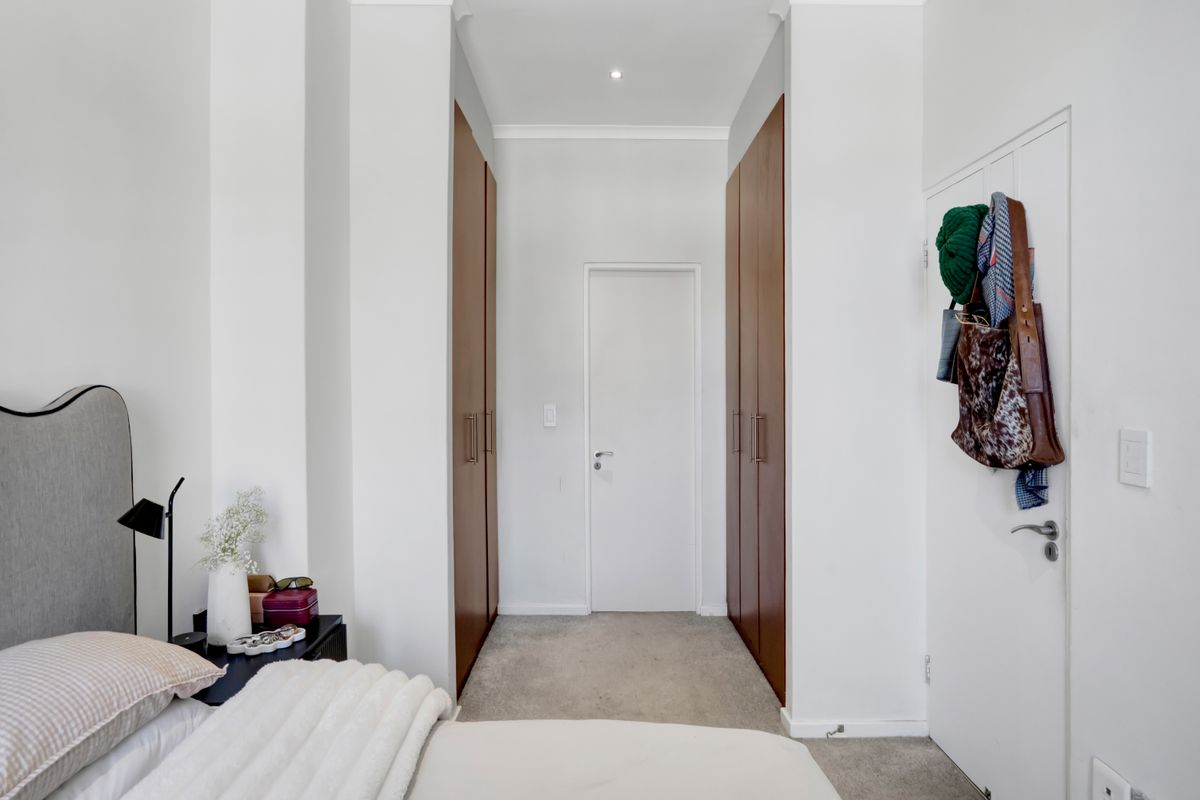 A well-maintained bedroom featuring built-in wooden cupboards, neutral carpeting, and clean white walls, providing a bright and functional living space.