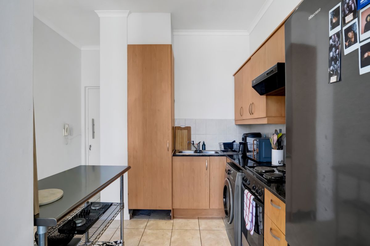 Compact kitchen featuring light wood cabinetry, dark countertops, tiled backsplash, and integrated appliances, offering a functional layout for apartment living.