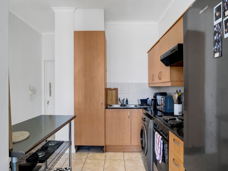 Compact kitchen featuring light wood cabinetry, dark countertops, tiled backsplash, and integrated appliances, offering a functional layout for apartment living.