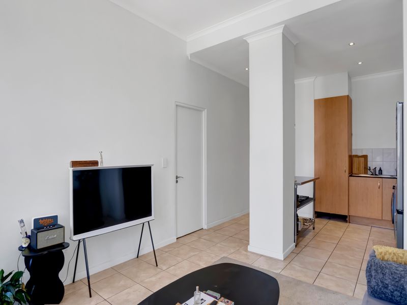 An open-plan living area featuring tiled flooring, a structural column, and a functional kitchen space with built-in cabinetry.