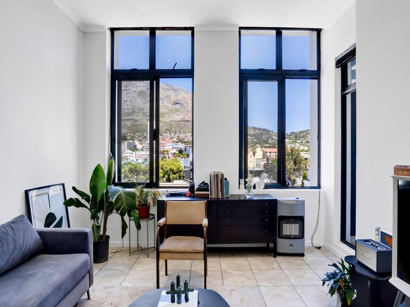 Bright living room featuring large windows with scenic mountain and city views, complemented by neutral tiled flooring and modern black window frames.