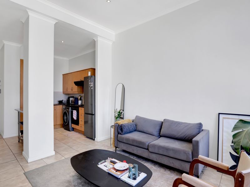 An open-plan living area featuring tiled flooring and a compact kitchen with built-in cabinetry and appliances, creating a functional and connected living space.