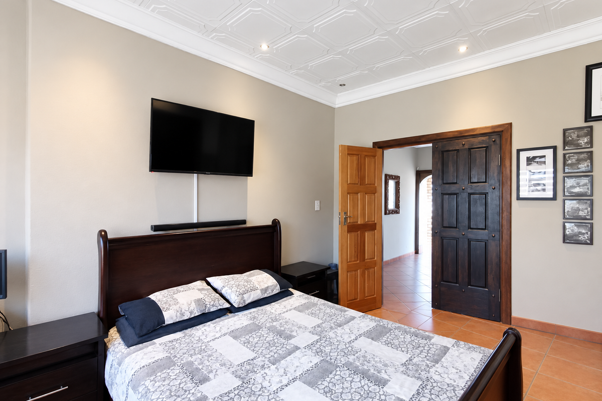 A well-maintained bedroom featuring a decorative coffered ceiling, recessed lighting, and elegant solid wood double doors leading to an adjacent tiled hallway.