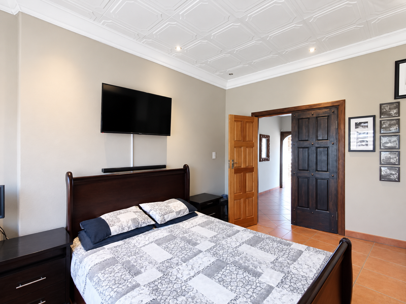 A well-maintained bedroom featuring a decorative coffered ceiling, recessed lighting, and elegant solid wood double doors leading to an adjacent tiled hallway.